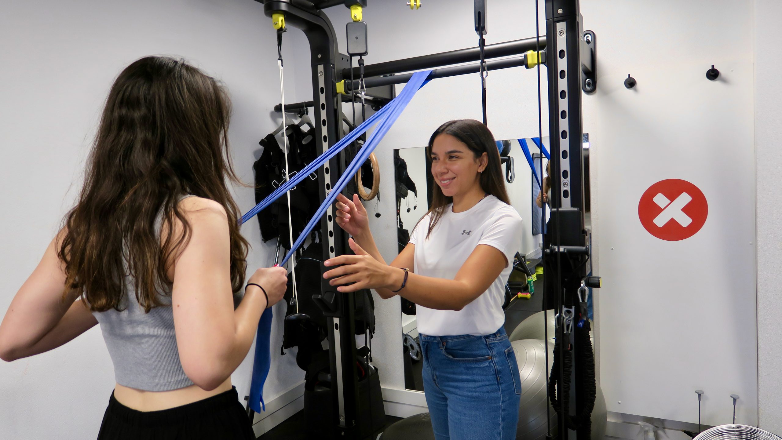 vrouw begeleid andere vrouw bij het sporten bij een fitnessaparaat