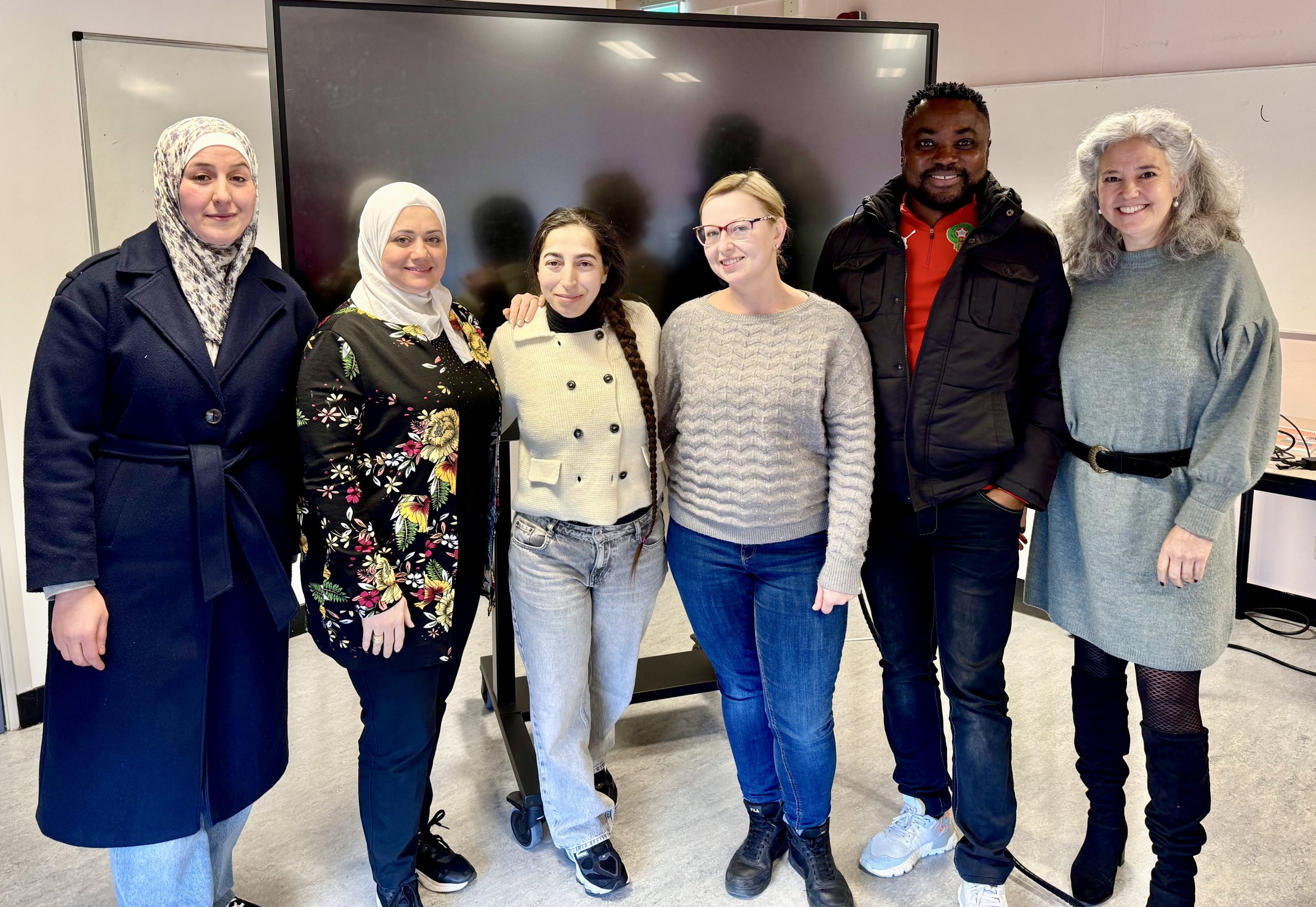 zes mensen voor een televisiescherm geposeerd