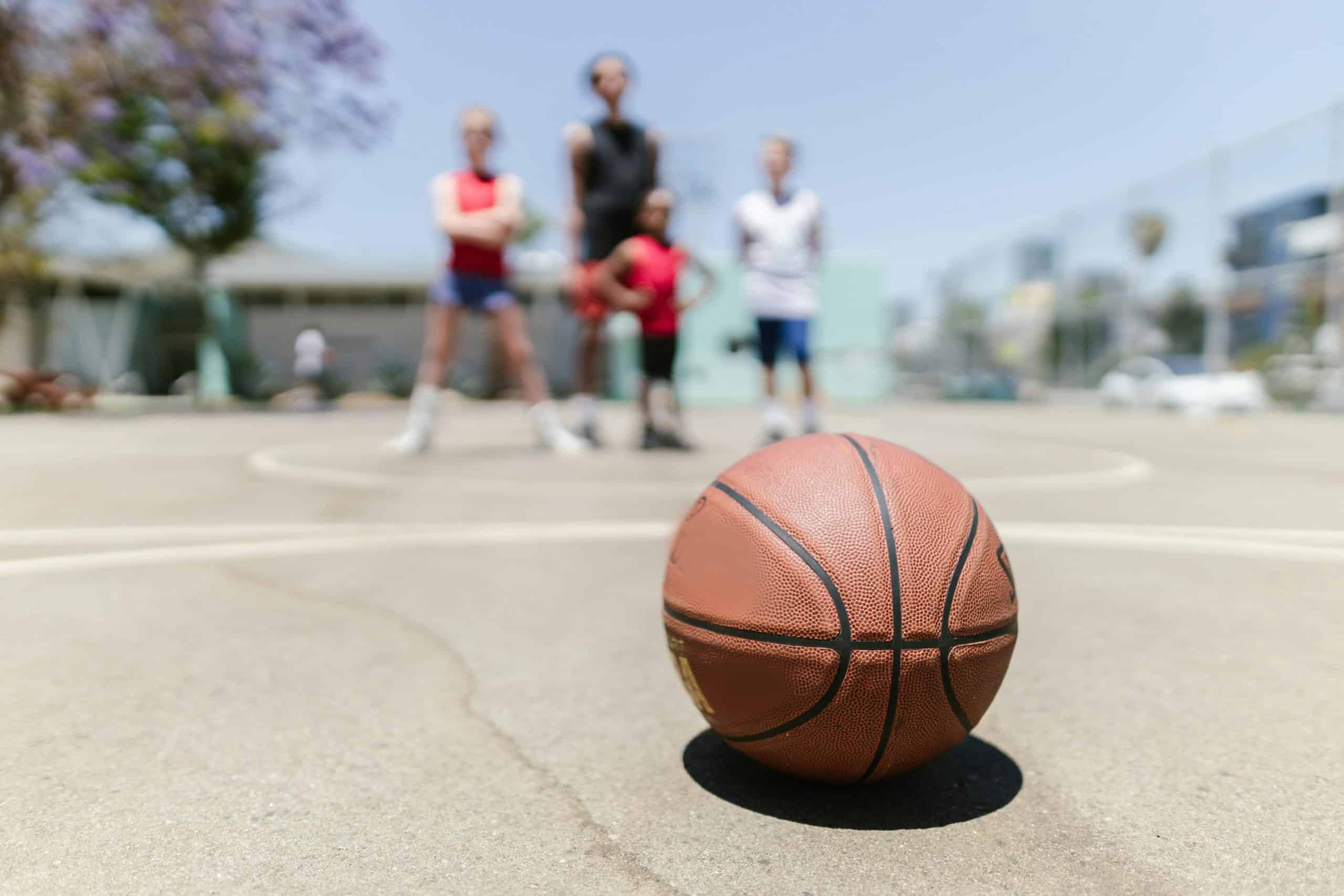 Op de voorgrond ligt een basketbal. Op de achtergrond zien we een aantal kinderen.