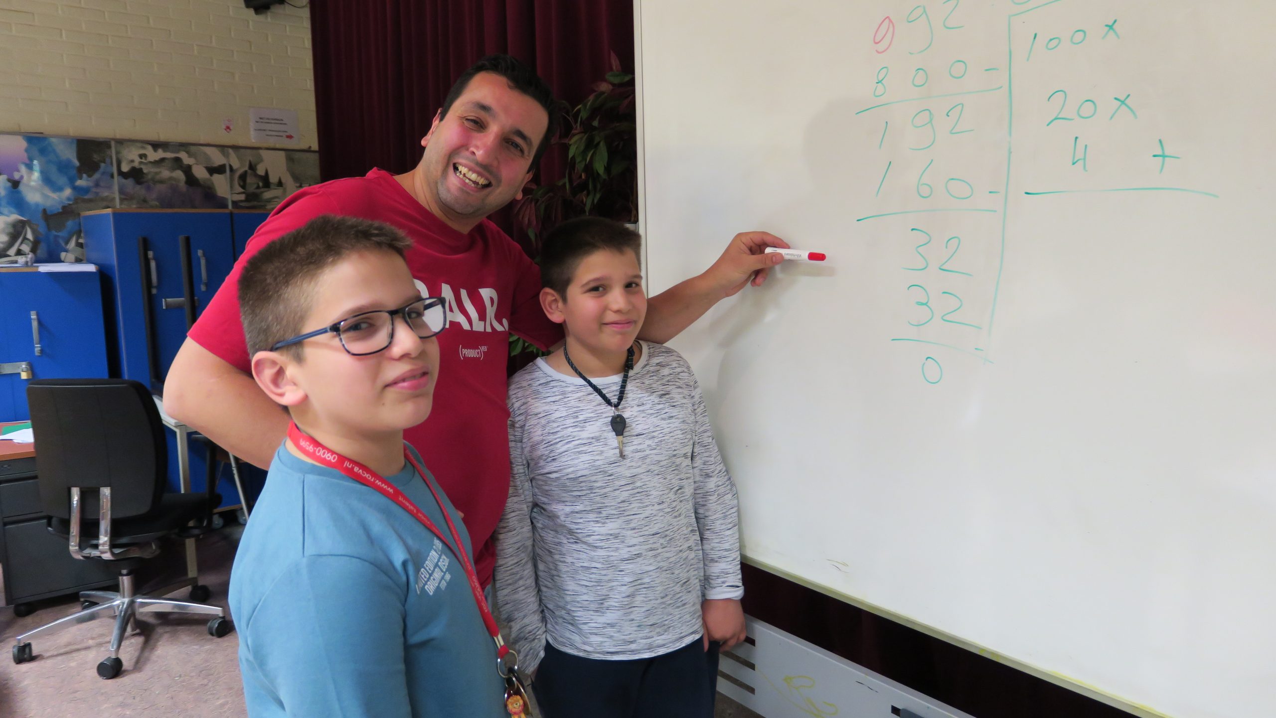 Meester helpt twee kinderen bij het bord met uitleg