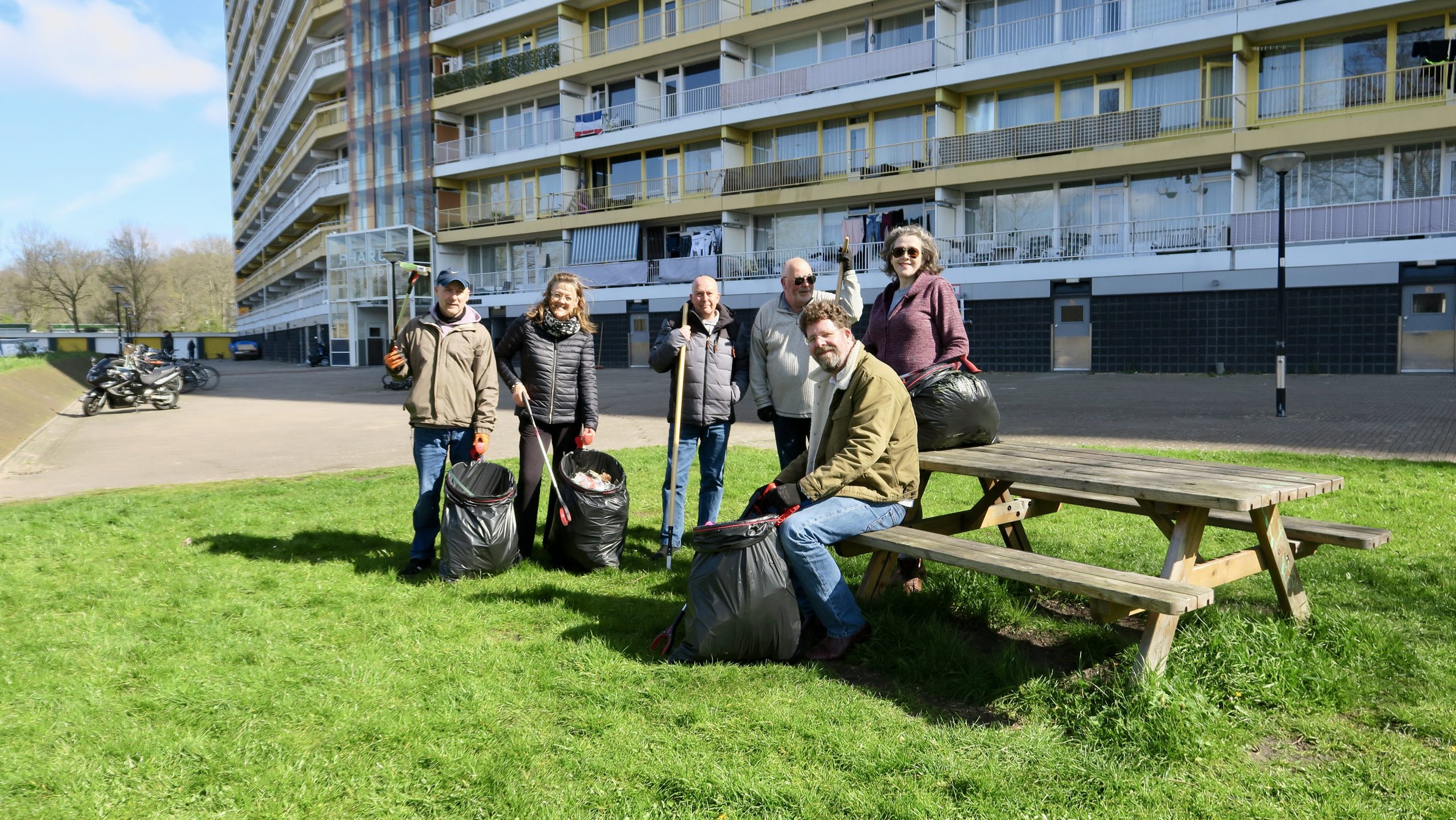 groepje volwassenen met prikstokken en een vuilniszak poserend