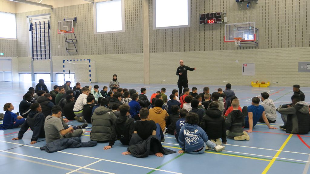 groep kinderen in een sportzaal toegesproken door een coach