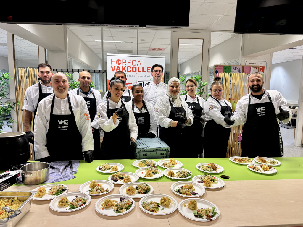 Groep mensen met schort achter een tafel met borden eten