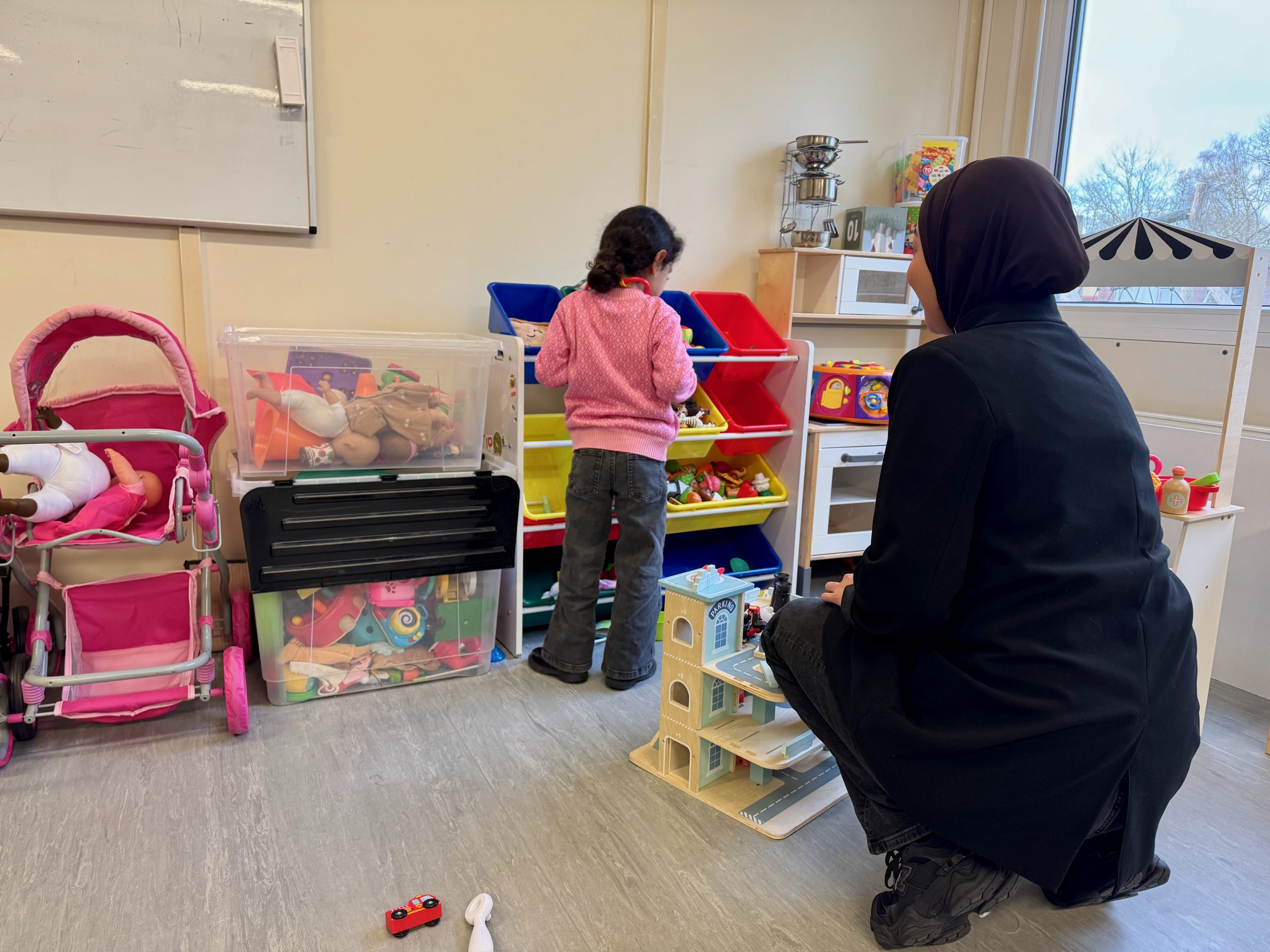 Vrouw knielt bij peuter in een speelzaal